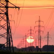 black transmission towers of power grid in front of orange-red sunset